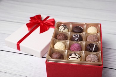 Photo of Red box with tasty chocolate candies on white wooden table, closeup