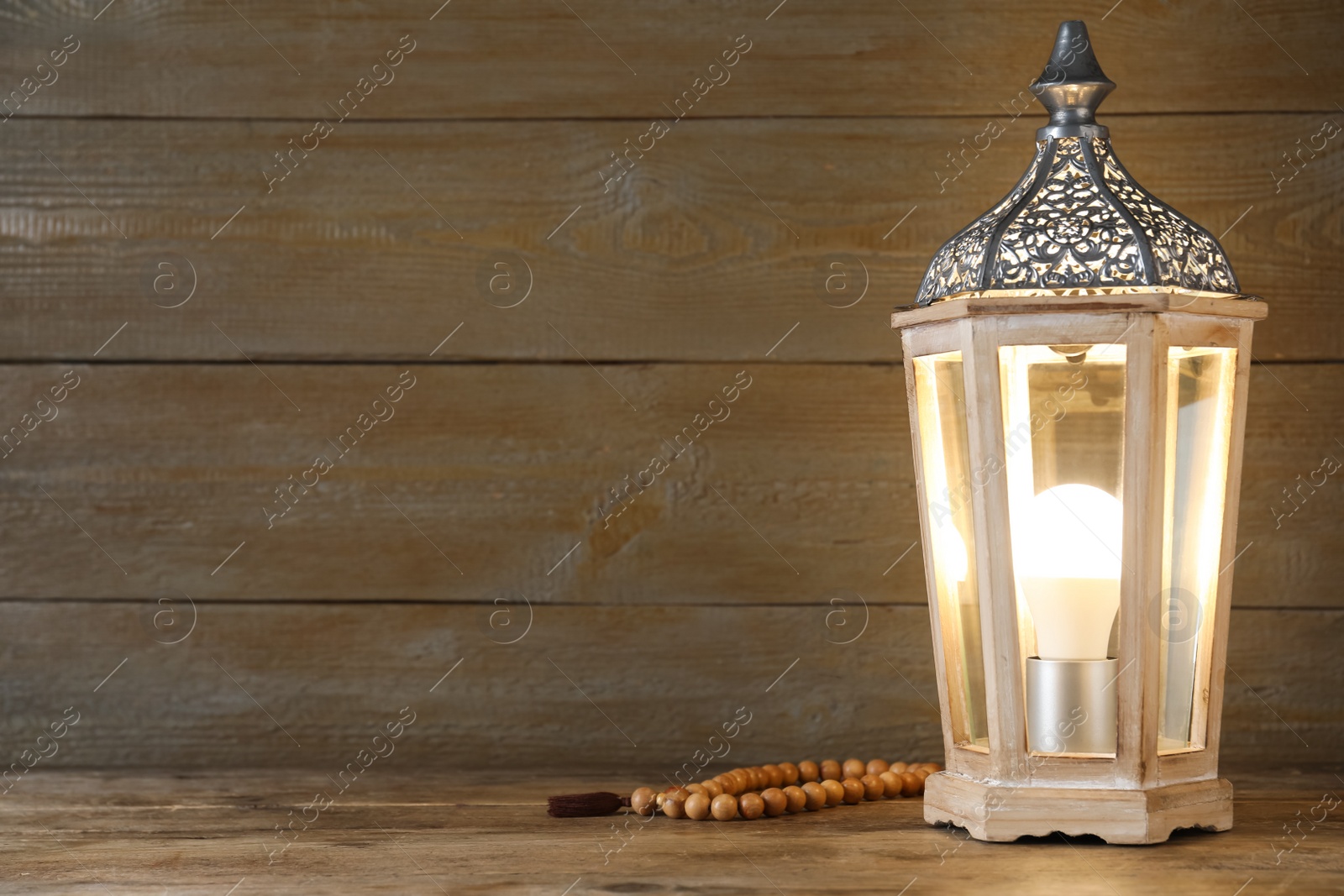 Photo of Decorative Arabic lantern and prayer beads on wooden table. Space for text