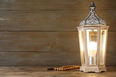 Decorative Arabic lantern and prayer beads on wooden table. Space for text