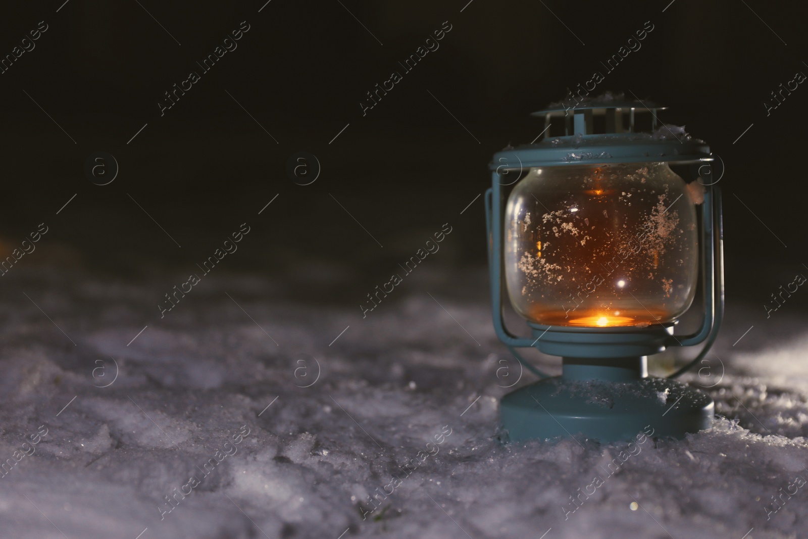 Photo of Lantern with burning candle on white snow outdoors. Space for text