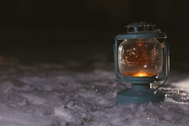 Photo of Lantern with burning candle on white snow outdoors. Space for text