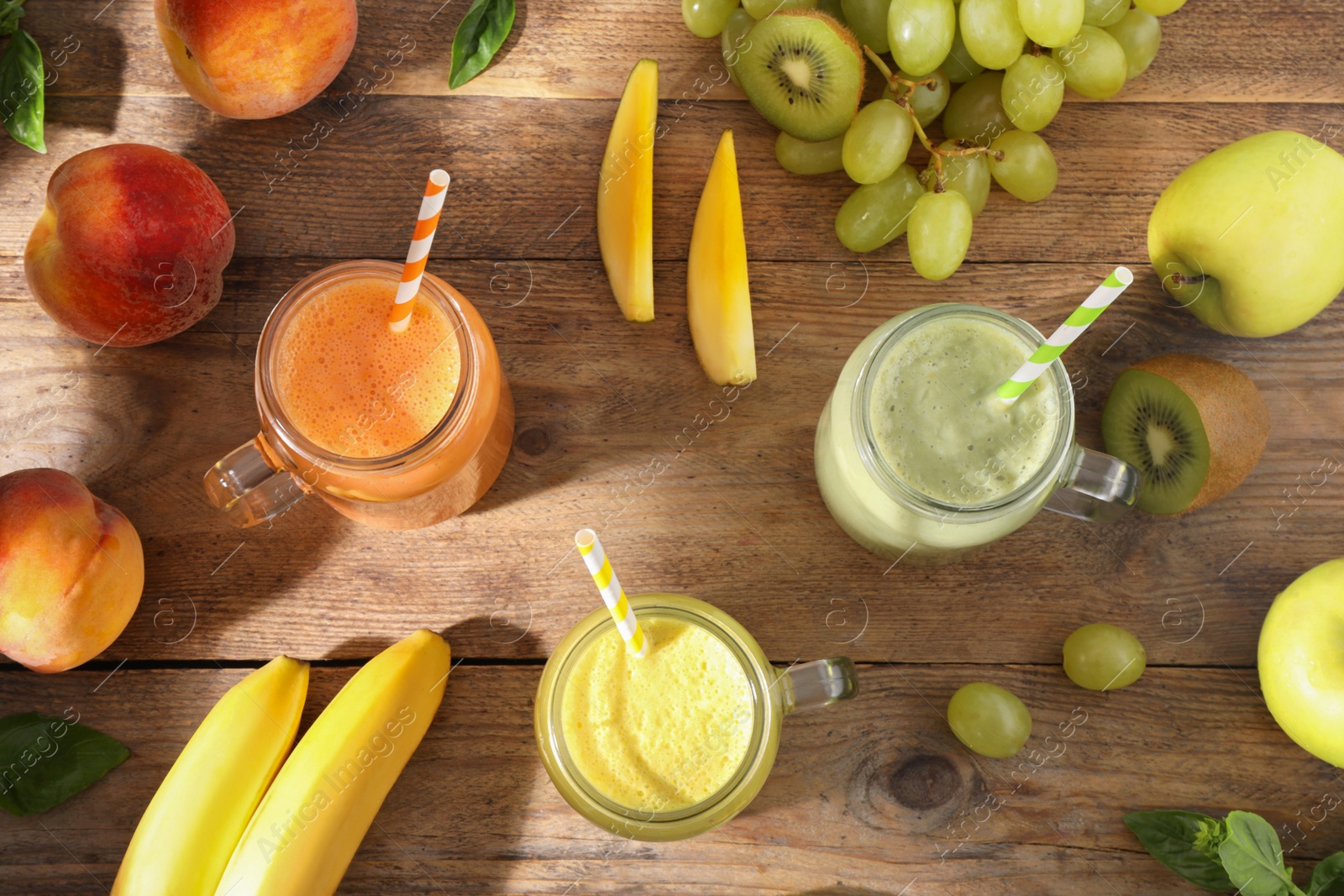 Photo of Mason jars of different tasty smoothies and fresh ingredients on wooden table, flat lay