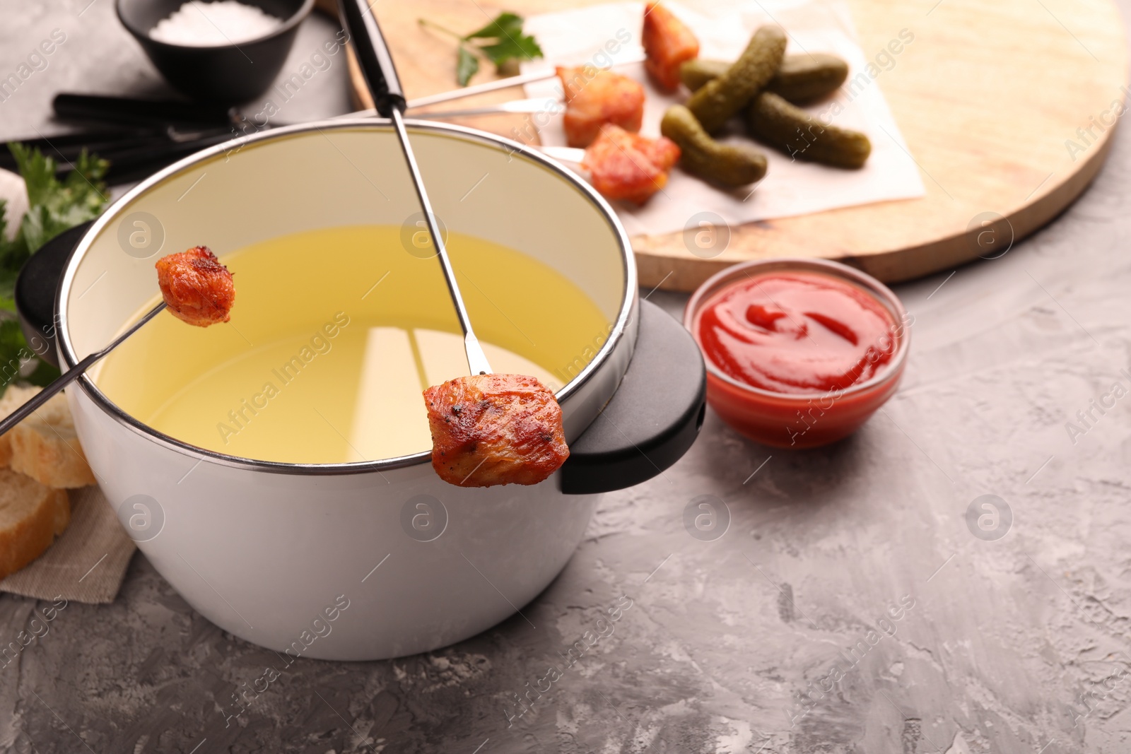 Photo of Fondue pot, forks with fried meat pieces, ketchup and other products on grey textured table. Space for text