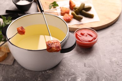 Fondue pot, forks with fried meat pieces, ketchup and other products on grey textured table. Space for text