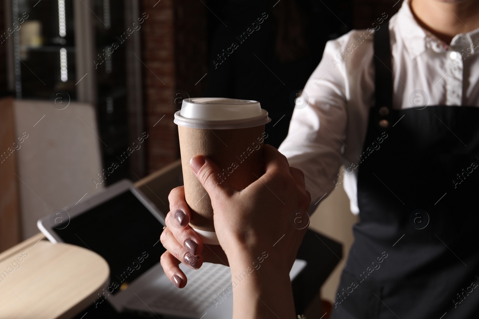 Photo of Barista giving takeaway paper cup with coffee to client in cafe, closeup