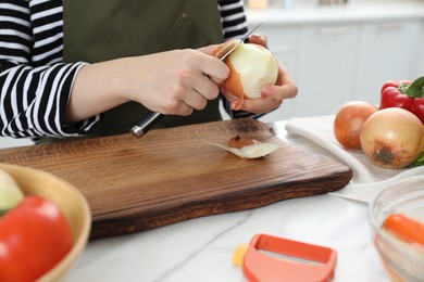 Woman peeling fresh onion with knife at white marble table indoors, closeup