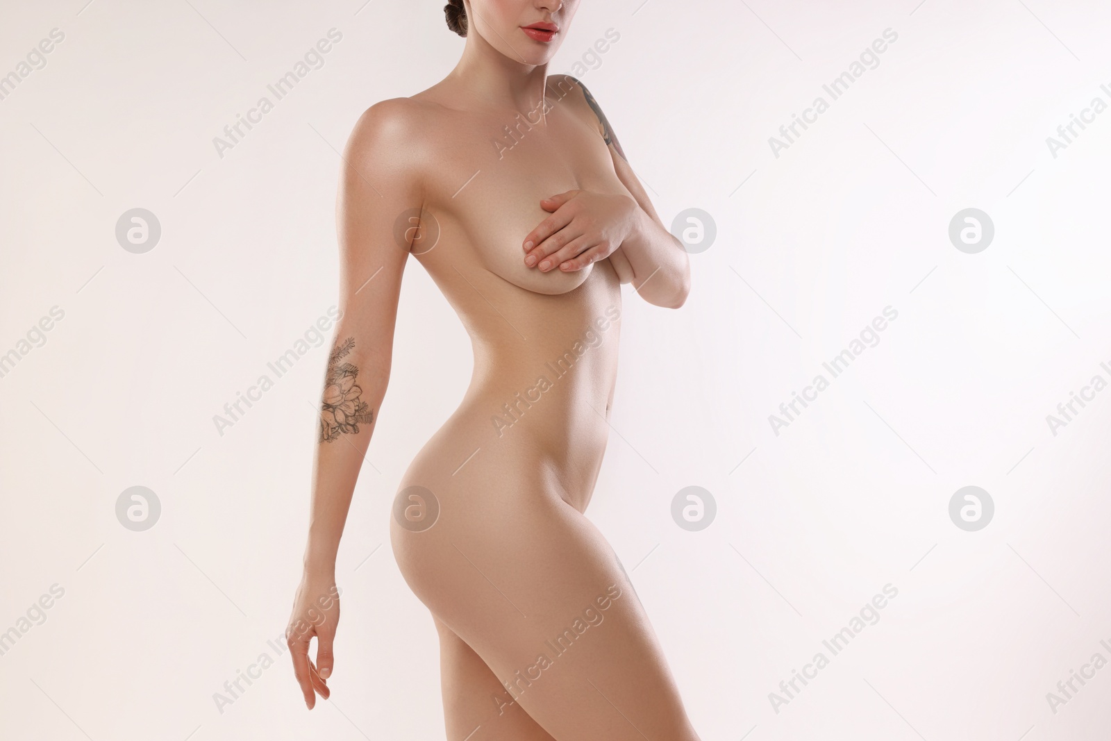 Photo of Nude woman with tattoos posing on white background, closeup