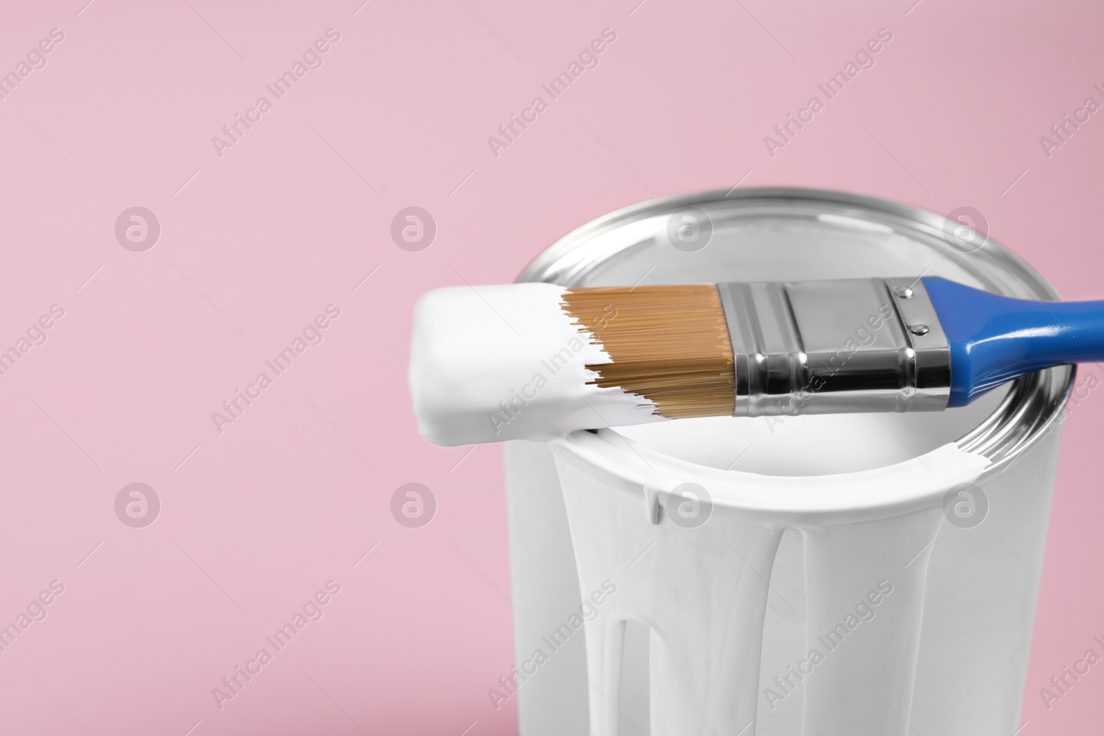 Photo of Can of white paint and brush on pink background, closeup. Space for text