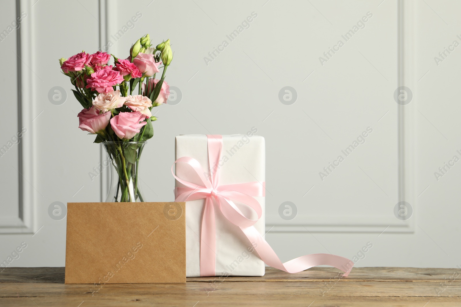 Photo of Happy Mother's Day. Gift box, blank card and bouquet of beautiful flowers in vase on wooden table near white wall. Space for text