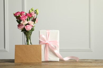 Happy Mother's Day. Gift box, blank card and bouquet of beautiful flowers in vase on wooden table near white wall. Space for text