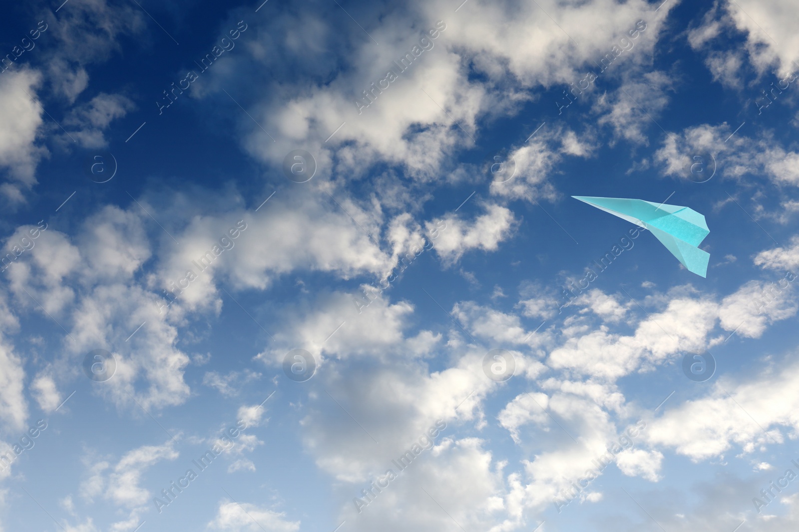 Image of Light blue paper plane flying in sky with clouds with clouds