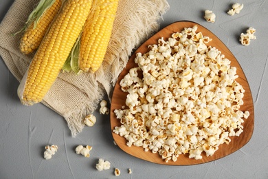 Plate with delicious popcorn and cobs on table, top view