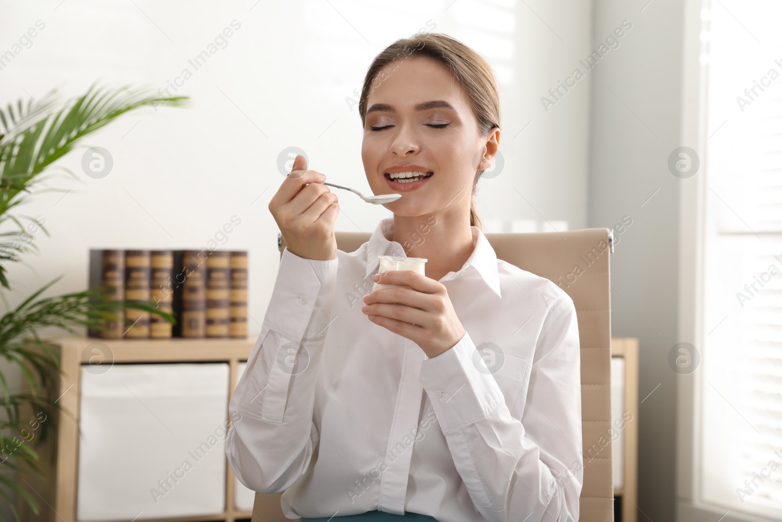 Photo of Young attractive woman eating tasty yogurt in office