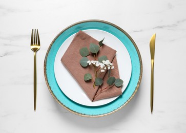 Stylish table setting with cutlery, flower and eucalyptus leaves, top view