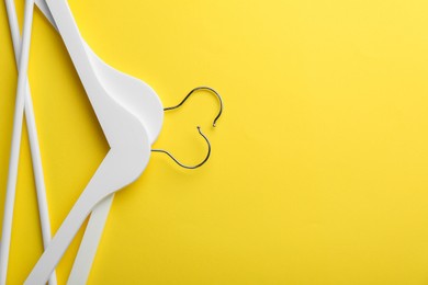 White hangers on yellow background, top view. Space for text