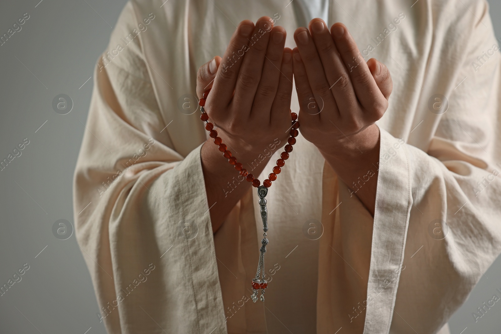 Photo of Muslim man with misbaha praying on light grey background, closeup