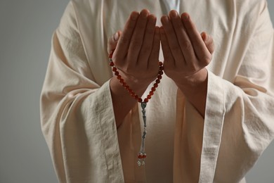 Photo of Muslim man with misbaha praying on light grey background, closeup