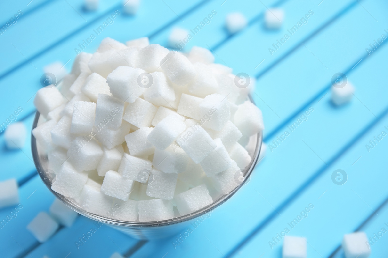 Photo of Bowl with refined sugar cubes on color wooden background