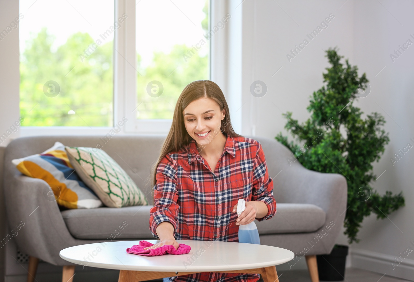 Photo of Young woman cleaning table with rag indoors