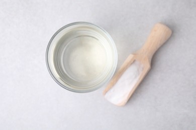 Photo of Vinegar in glass, baking soda and wooden scoop on light table, top view