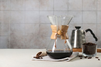 Photo of Glass chemex coffeemaker with tasty drip coffee and beans on white table. Space for text