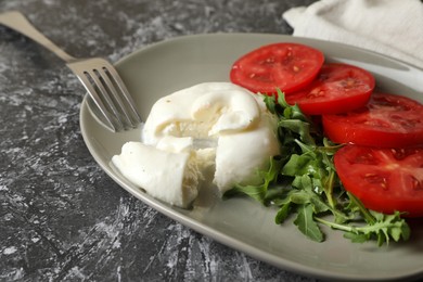 Photo of Delicious burrata cheese with tomatoes, arugula and fork on grey table, closeup