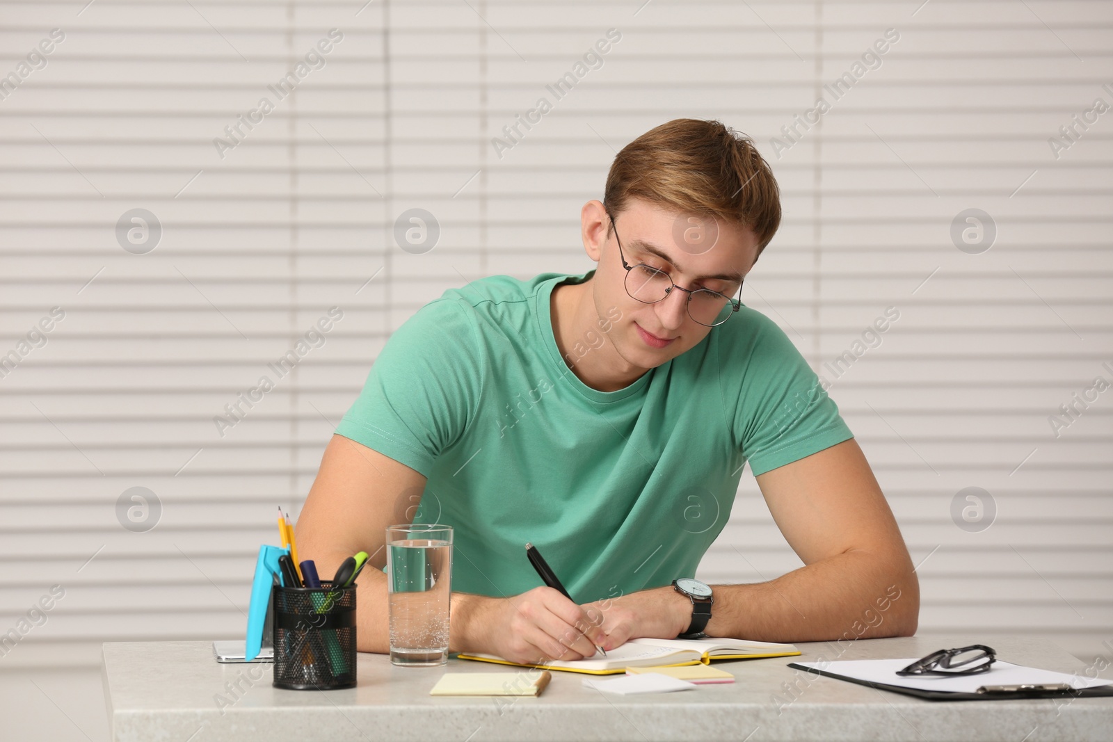 Photo of Young man writing in notebook at table indoors