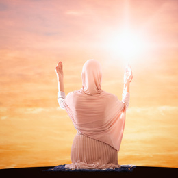 Image of Muslim woman in traditional clothes praying at sunrise, back view. Holy month of Ramadan