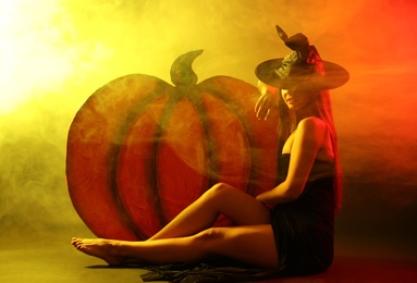 Photo of Young woman wearing witch costume near decorative pumpkin in smoke cloud. Halloween party