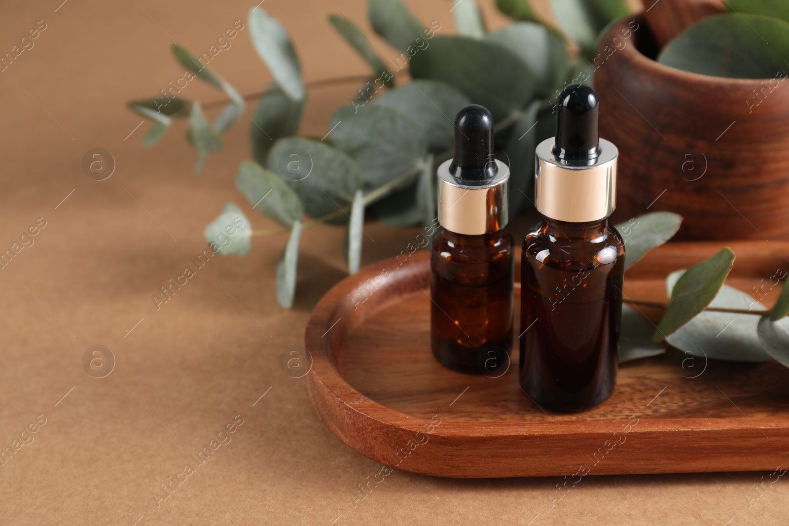 Photo of Aromatherapy. Bottles of essential oil and eucalyptus leaves on brown table, closeup. Space for text