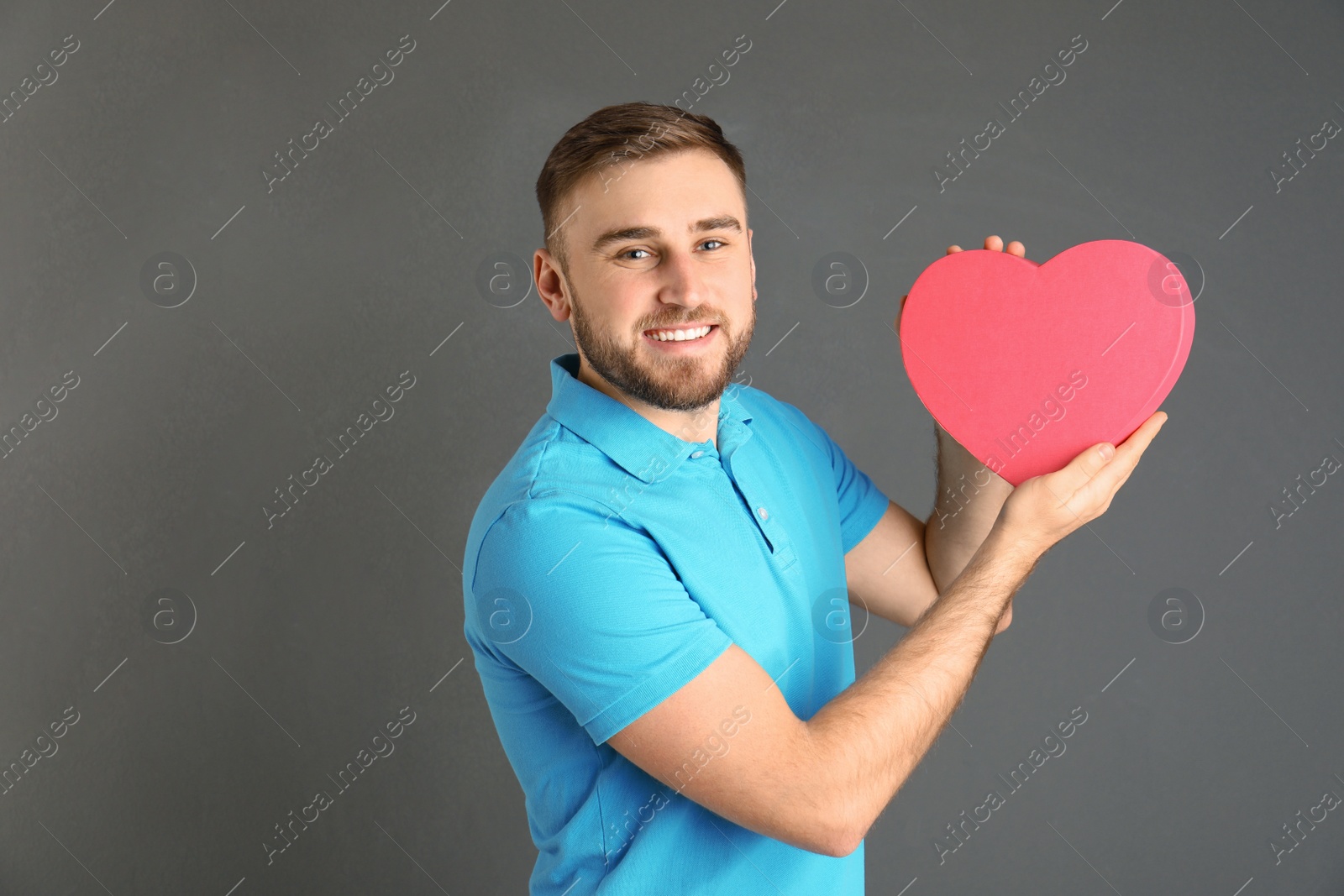 Photo of Young man with heart shaped box on grey background