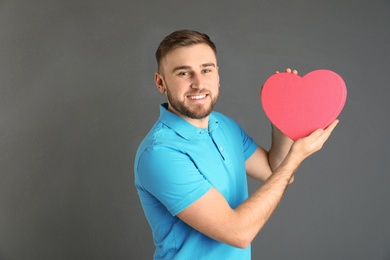 Photo of Young man with heart shaped box on grey background