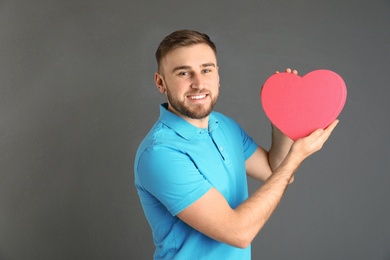 Young man with heart shaped box on grey background