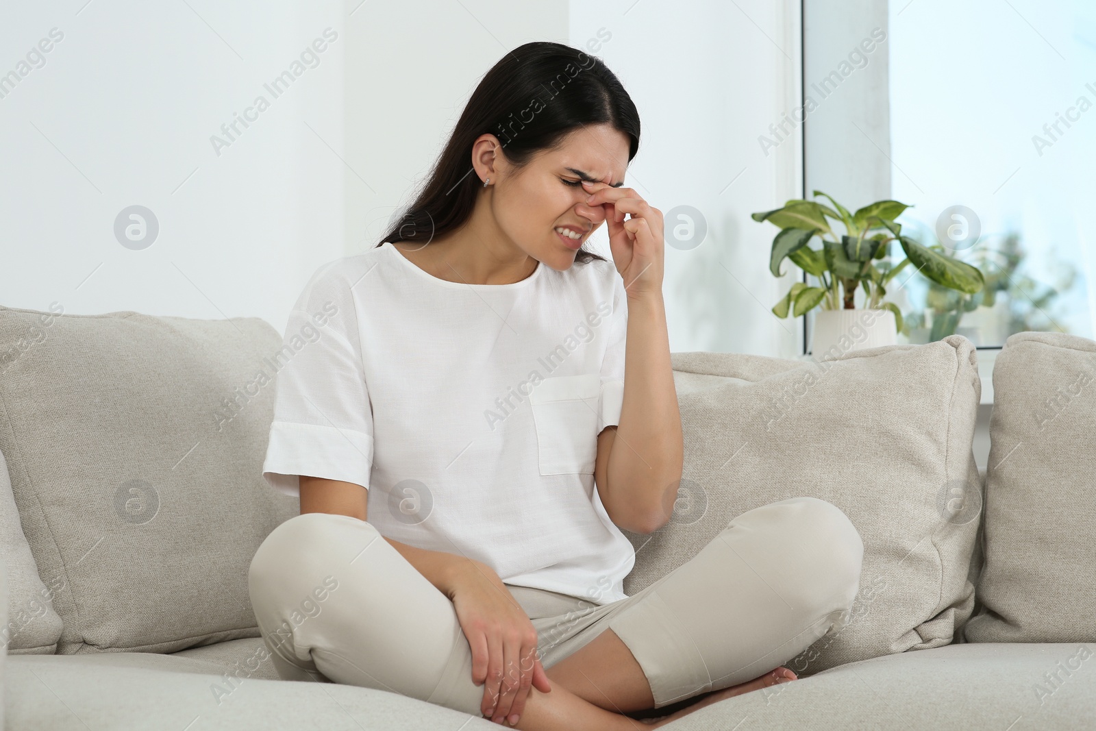 Photo of Young woman suffering from headache on sofa at home. Hormonal disorders