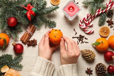 Photo of Woman decorating tangerine with cloves at light wooden table, top view. Christmas atmosphere