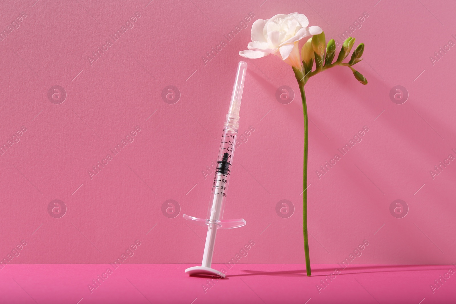 Photo of Cosmetology. Medical syringe and freesia flower on pink background