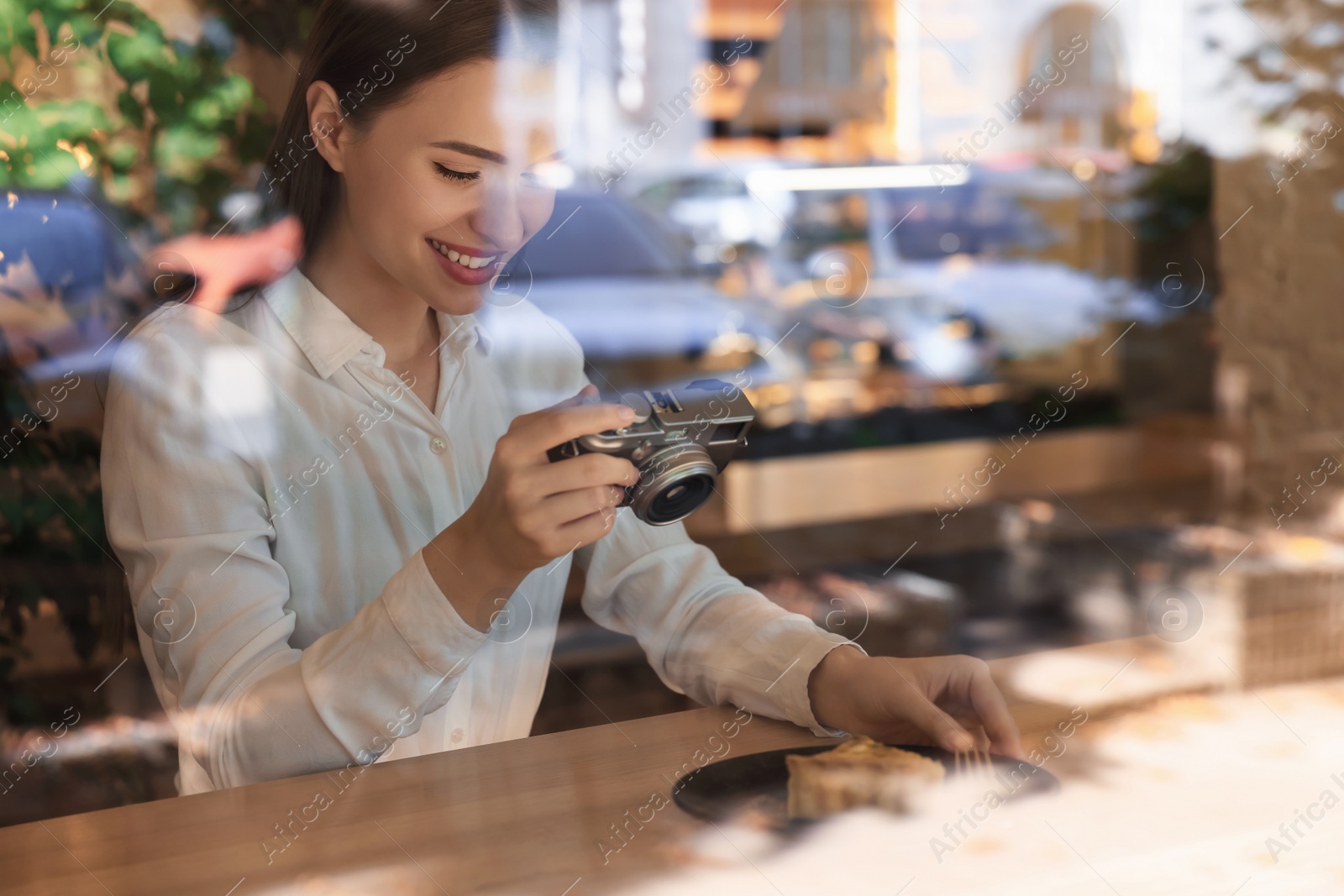 Photo of Young woman taking photo of plate with pie at cafe, view through window. Creative hobby