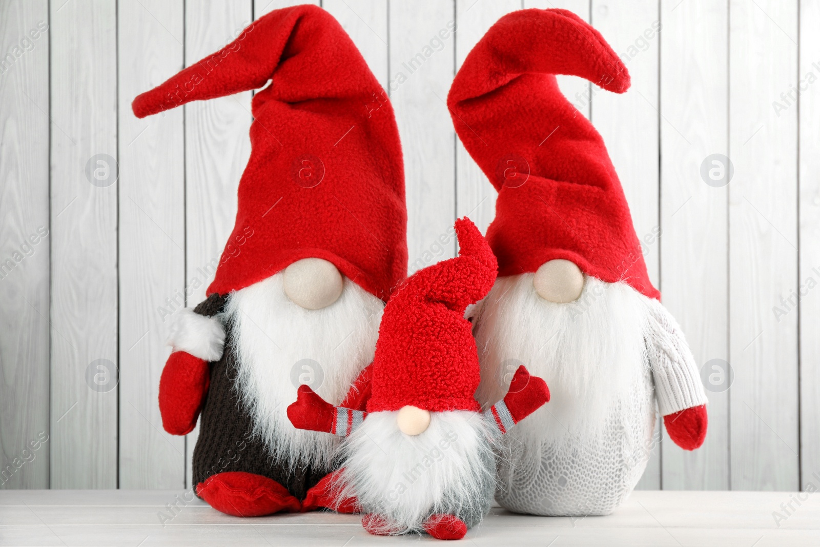 Photo of Cute Christmas gnomes on table against white wooden background