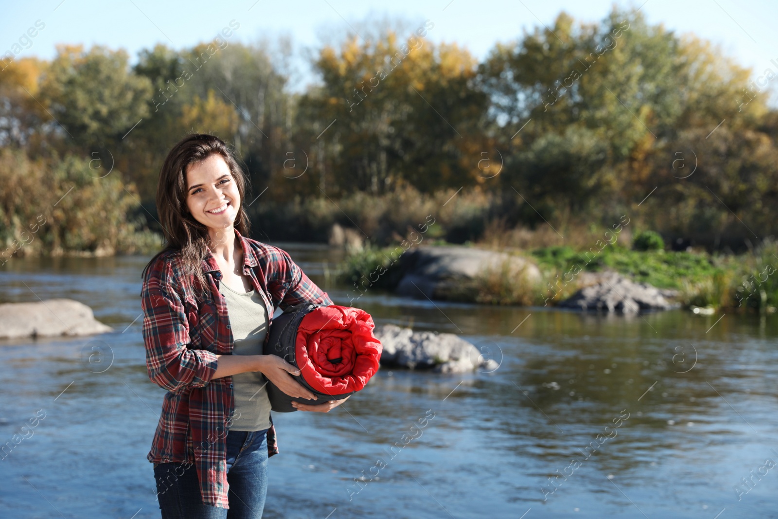 Photo of Female camper with sleeping bag near pond. Space for text