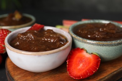 Photo of Tasty rhubarb jam in bowls and strawberries on table, closeup