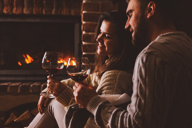 Photo of Lovely couple with glasses of wine near fireplace at home. Winter vacation