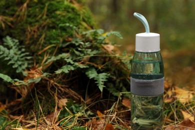 Glass bottle of fresh water on ground in forest, space for text