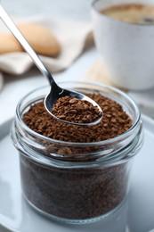 Photo of Instant coffee and spoon above glass jar on table, closeup