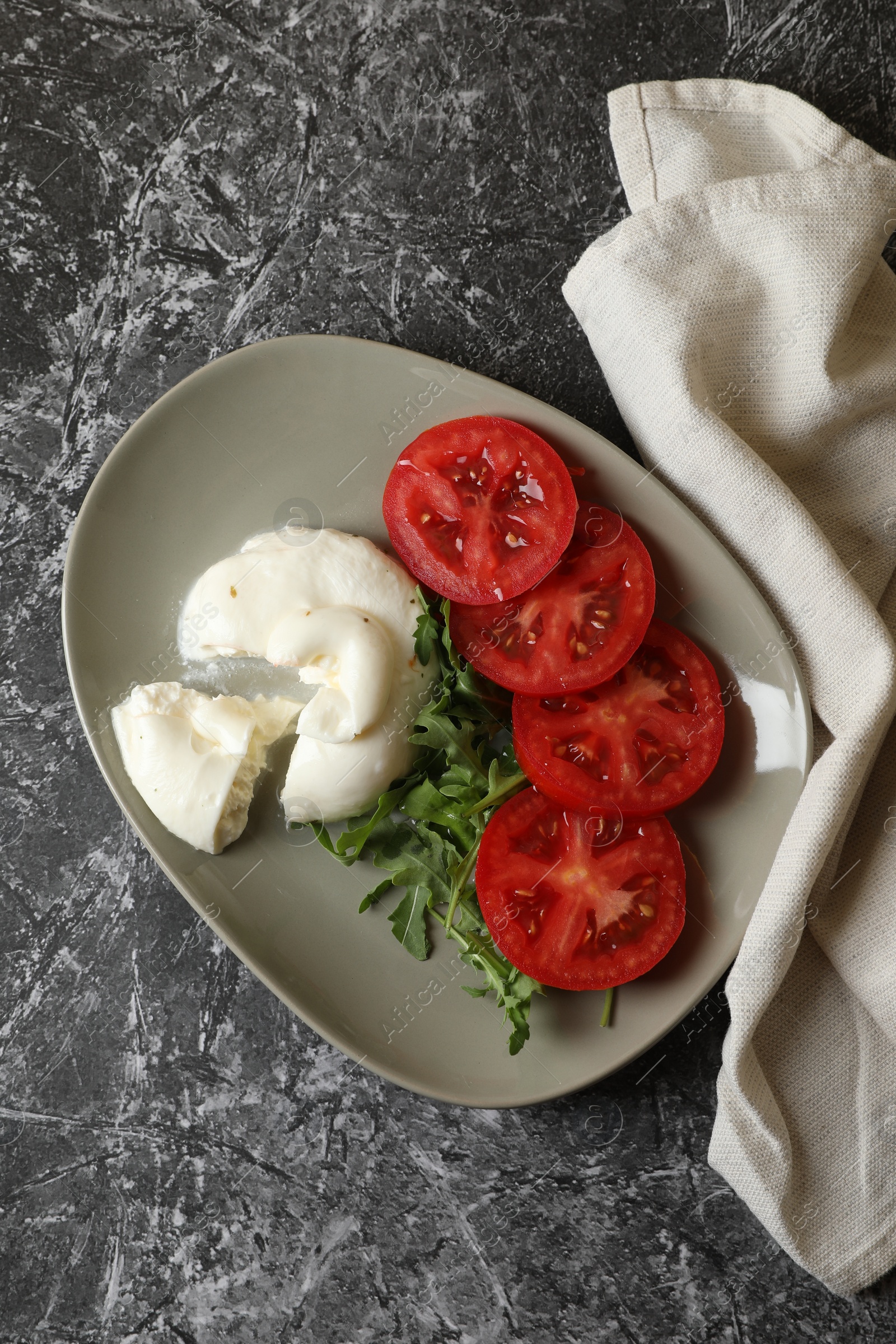 Photo of Delicious burrata cheese with tomatoes and arugula on grey table, flat lay