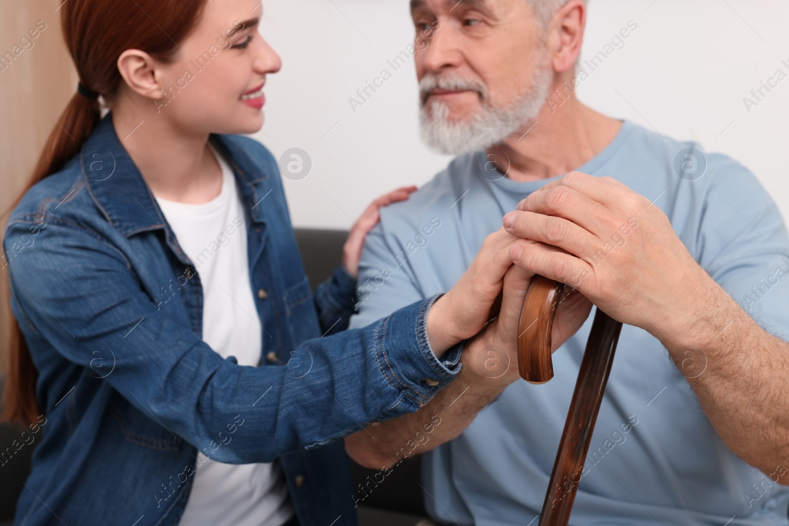 Photo of Caregiver and senior man with walking cane on sofa at home, selective focus