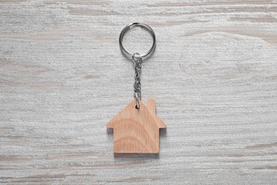 Photo of One keychain in shape of house on light wooden table, top view