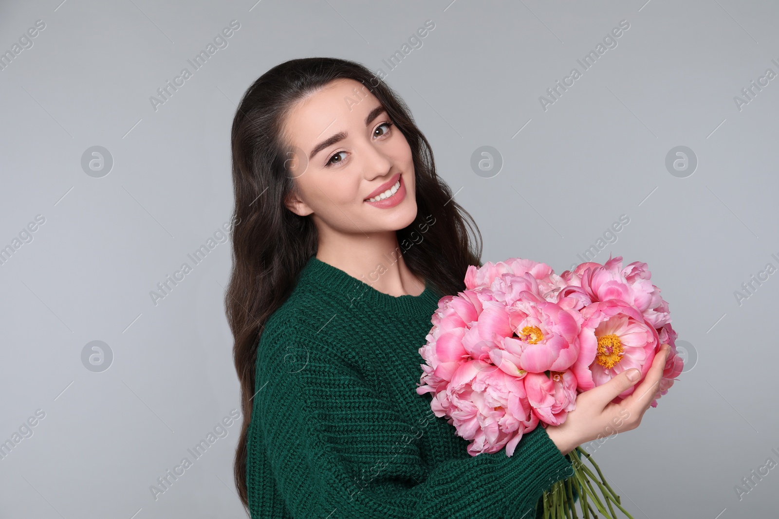 Photo of Beautiful young woman with bouquet of peonies on light grey background