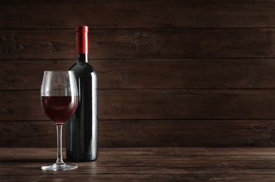 Photo of Glass and bottle with delicious red wine on table against dark background