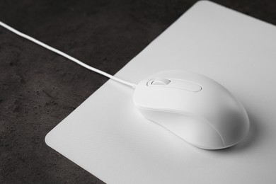 Photo of Wired mouse with mousepad on black textured table, closeup