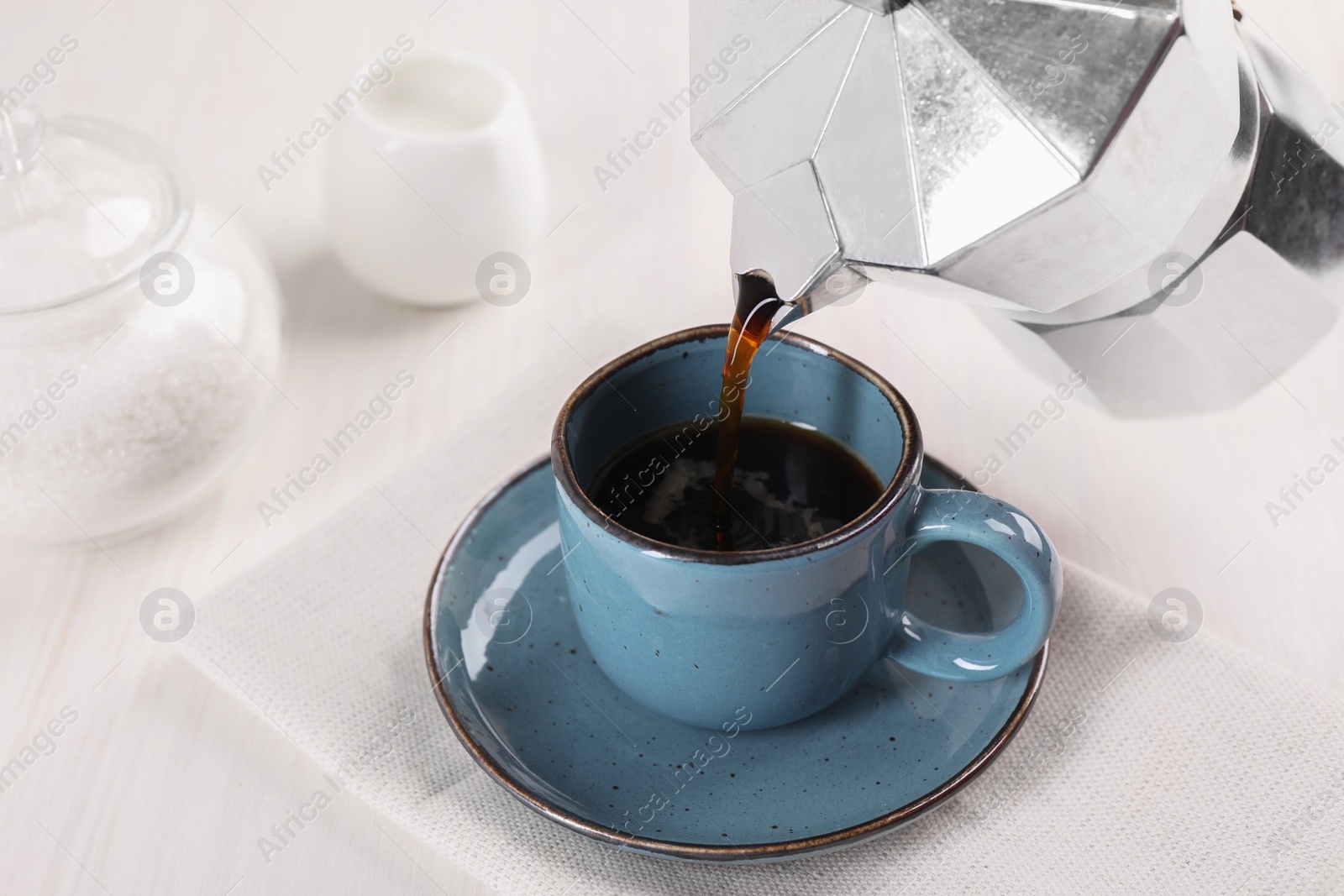 Photo of Pouring aromatic coffee from moka pot into cup at white wooden table, closeup